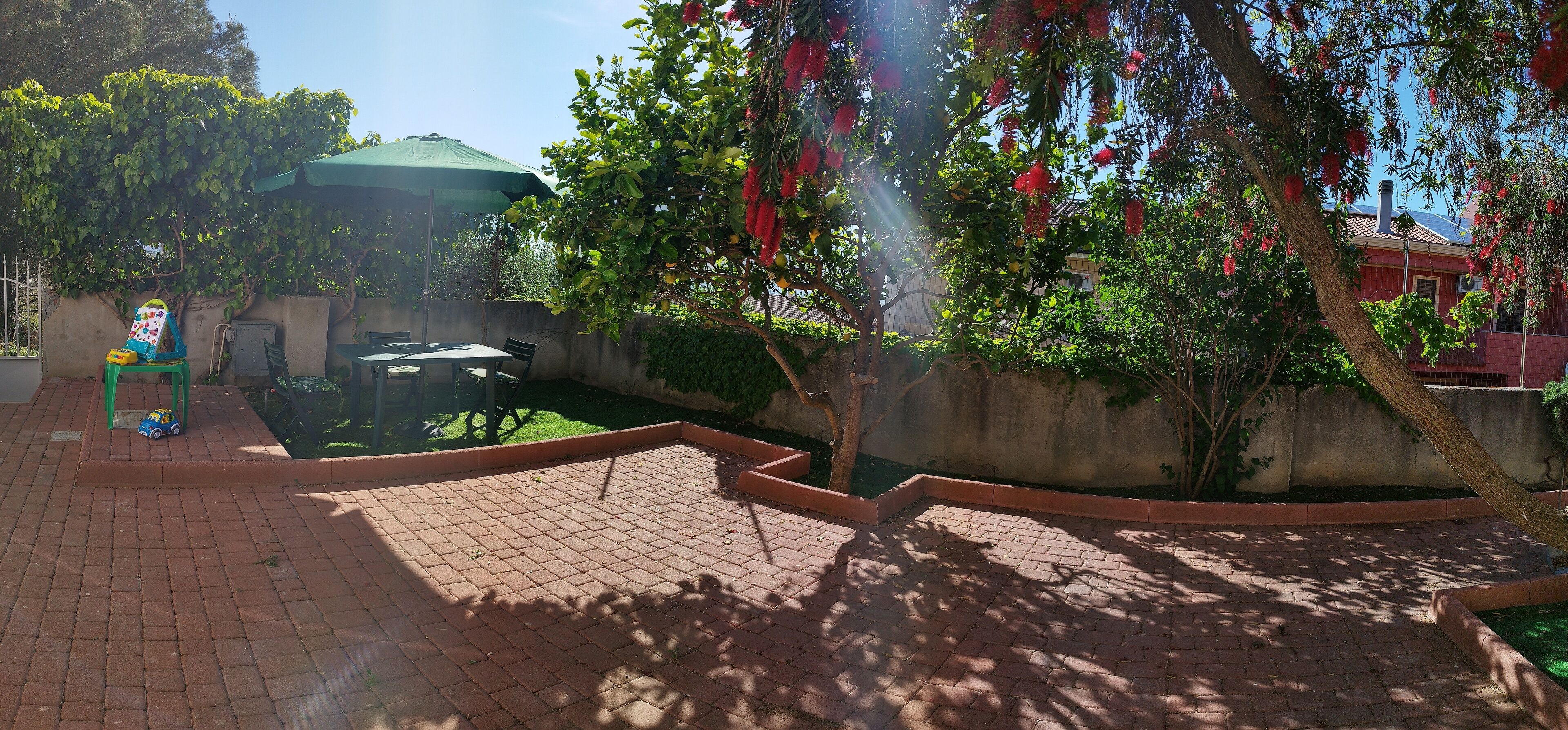 A patio area with a brick floor, a green umbrella, and a small table with chairs.