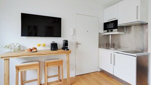 A compact kitchen with a TV, microwave, and stainless steel appliances. There are two wooden stools and a small table with breakfast items. - Charming Apartment - 1br-4p- Suresnes (Suresnes)