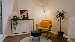 A corner room with a yellow armchair, a round black ottoman, a potted plant, a framed picture, and a floor lamp. - Modern Apartment in Koblenz (Koblenz)