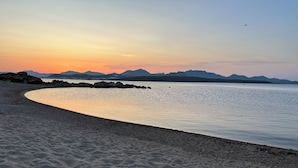 Una spiaggia con un litorale curvilineo, acqua calma e montagne sullo sfondo.