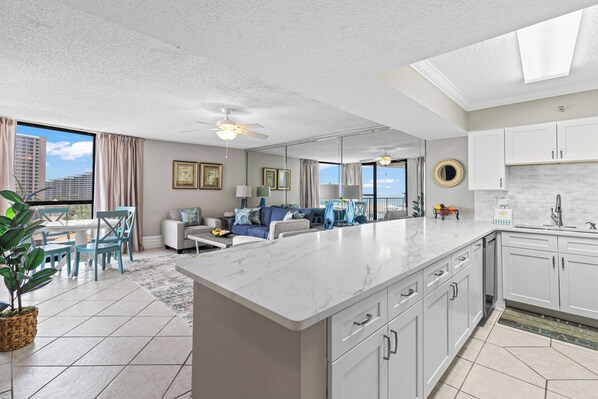 A modern kitchen with white cabinets, a marble countertop, and a dining area with blue chairs.