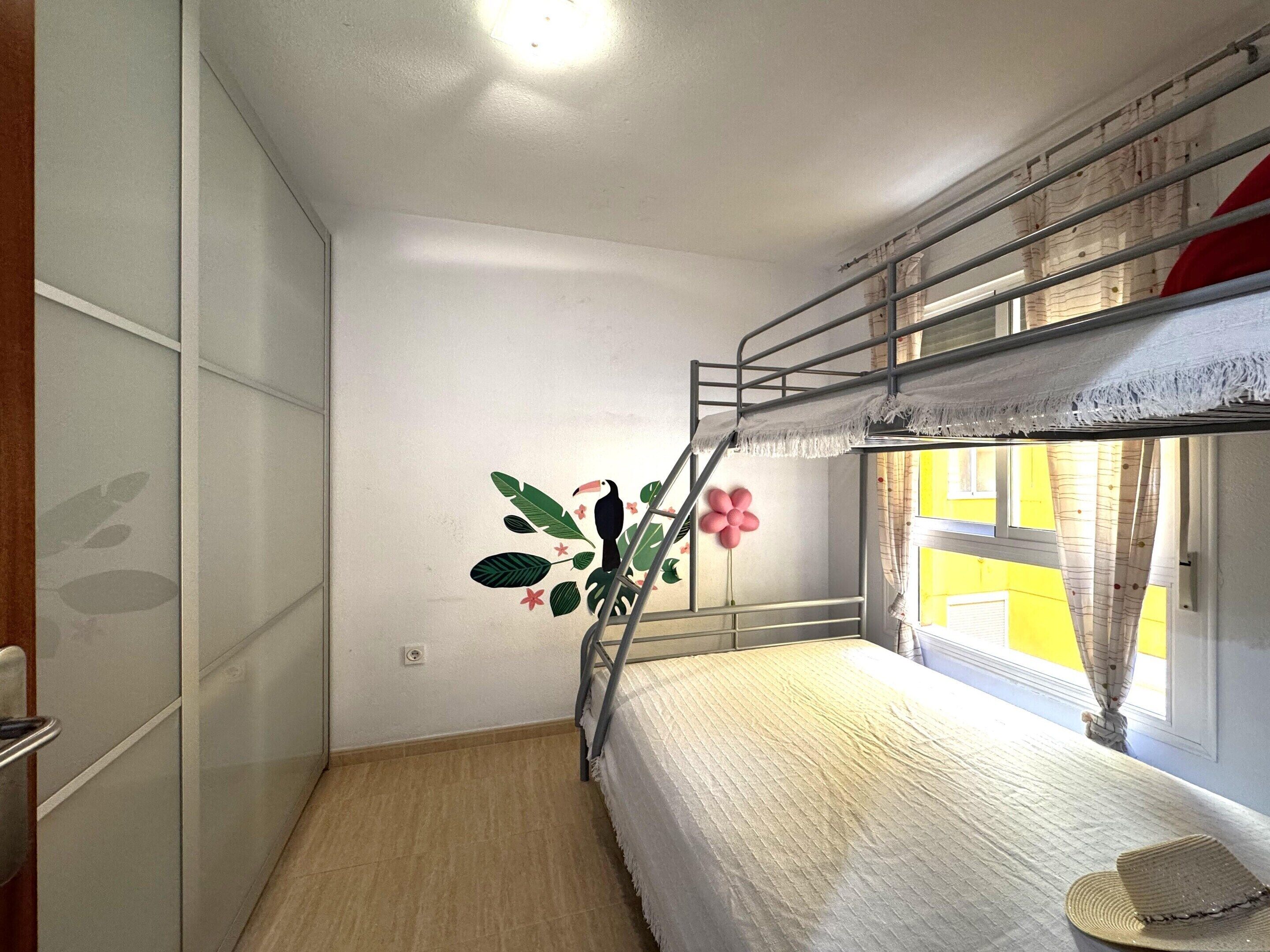 A bunk bed room with a ladder, a wall decoration of a toucan and flowers, and a window with curtains.
