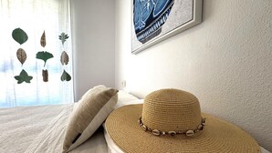 A bed with a woven hat and a pillow, a wall with a framed artwork, and a window with leaf patterns. - Premium Apartment in Roquetas de Mar (Roquetas de Mar)