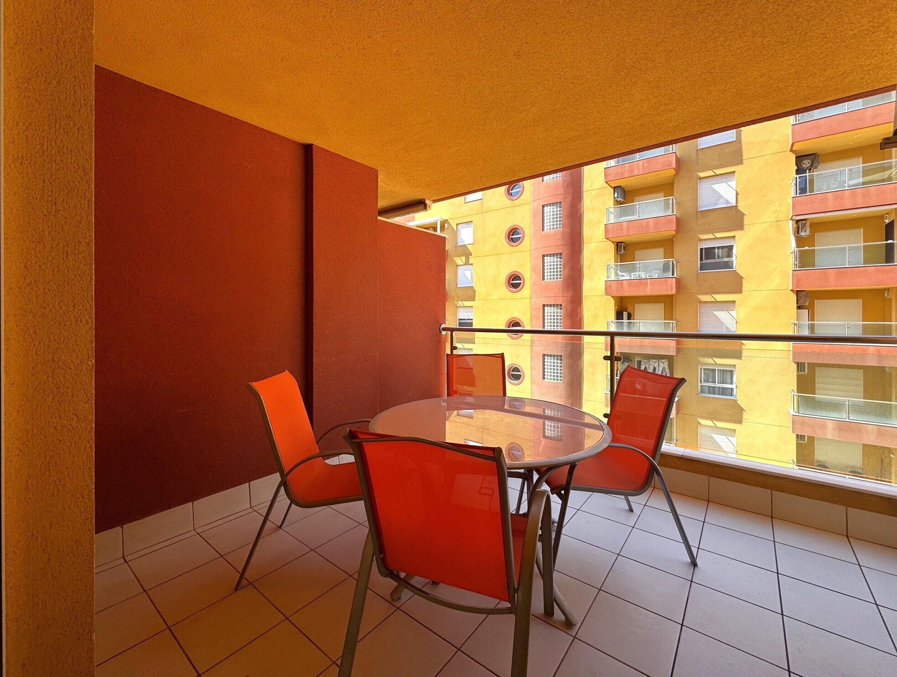 Un balcone con ringhiera in vetro, sedie arancioni e un tavolino in vetro.