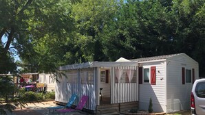 A mobile home with a porch, a small attached structure, and a car parked nearby. - Rent MOBILHOME air-conditioned quiet terrace covered bicycles 10mn beach LA TREMBLADE (La Tremblade)