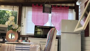 A room with a bed, a table with a vase of flowers, a refrigerator, and a window with pink curtains. - Rent MOBILHOME air-conditioned quiet terrace covered bicycles 10mn beach LA TREMBLADE (La Tremblade)