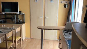 A compact kitchen with a dining area, wooden flooring, a TV, and a stove. - Rent MOBILHOME air-conditioned quiet terrace covered bicycles 10mn beach LA TREMBLADE (La Tremblade)