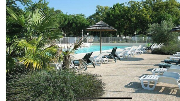 A poolside area with lounge chairs and umbrellas, surrounded by greenery. - Rent MOBILHOME air-conditioned quiet terrace covered bicycles 10mn beach LA TREMBLADE (La Tremblade)