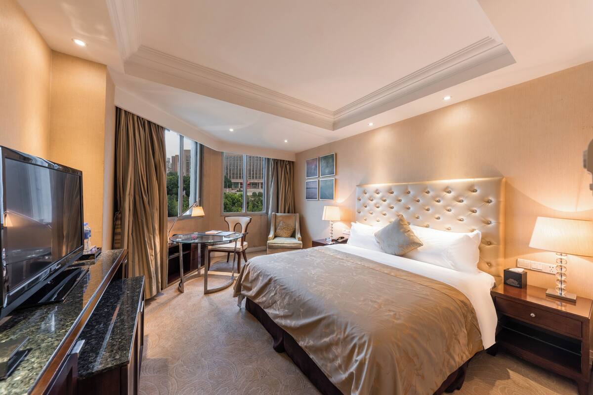 A hotel room with a large bed, a TV, a desk, and a chair.