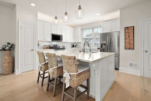 A modern kitchen with white cabinetry, a central island with bar stools, stainless steel appliances, and pendant lighting.