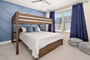 Una cama litera con edredón blanco, almohadas azules y un ventilador de techo.
