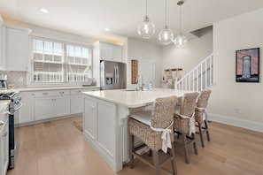 A modern kitchen with white cabinetry, a large island, wicker bar stools, and pendant lighting.