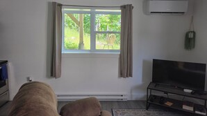 A living room with a large window, a flat-screen TV, a sofa, and a small table with a remote control. - A Gorgeous 1bedroom Walkout Basement in a Serene Environment (Halifax)