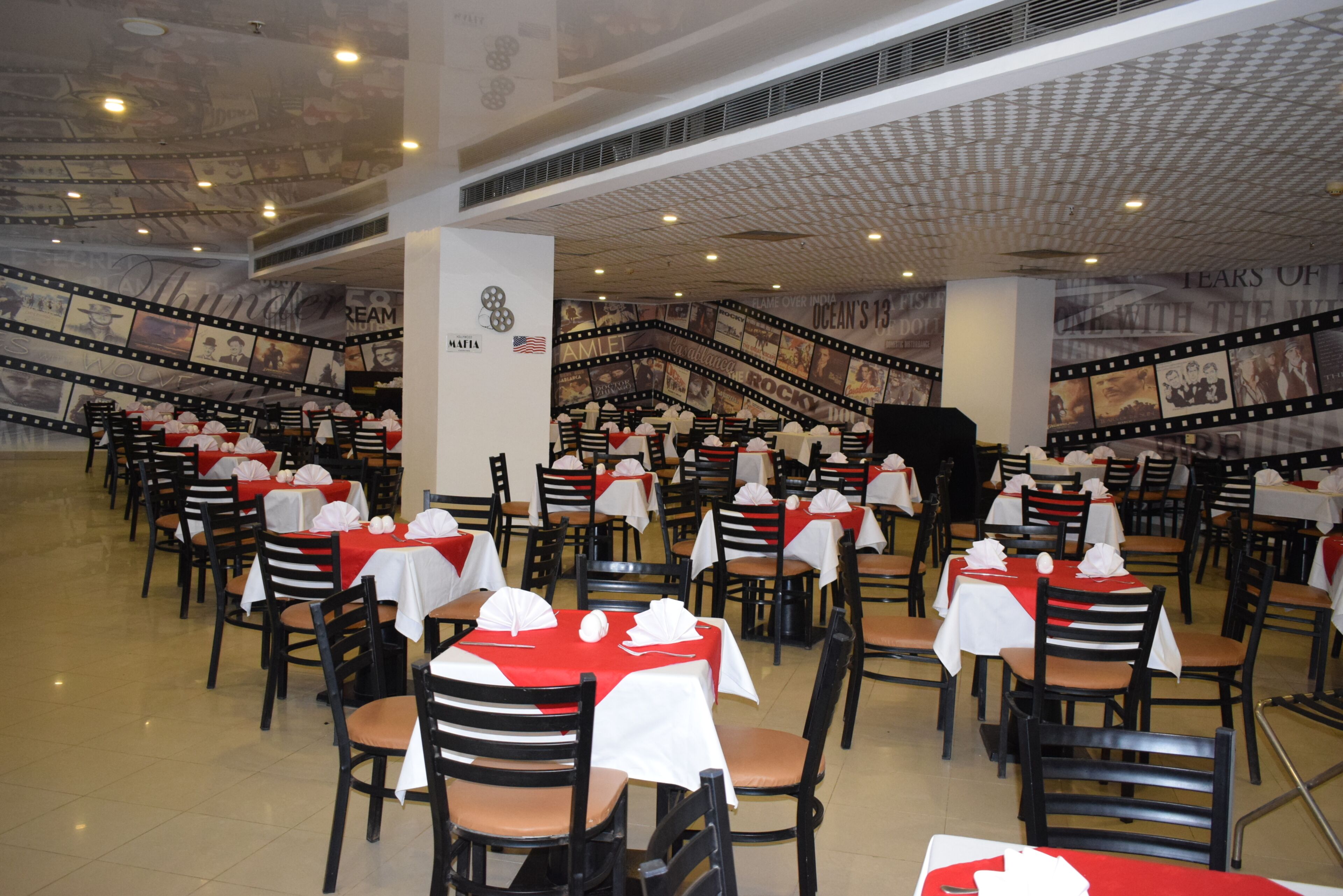 Un amplio comedor interior con numerosas mesas y sillas, techo con diseño y paredes decoradas con diversas imágenes y texto.