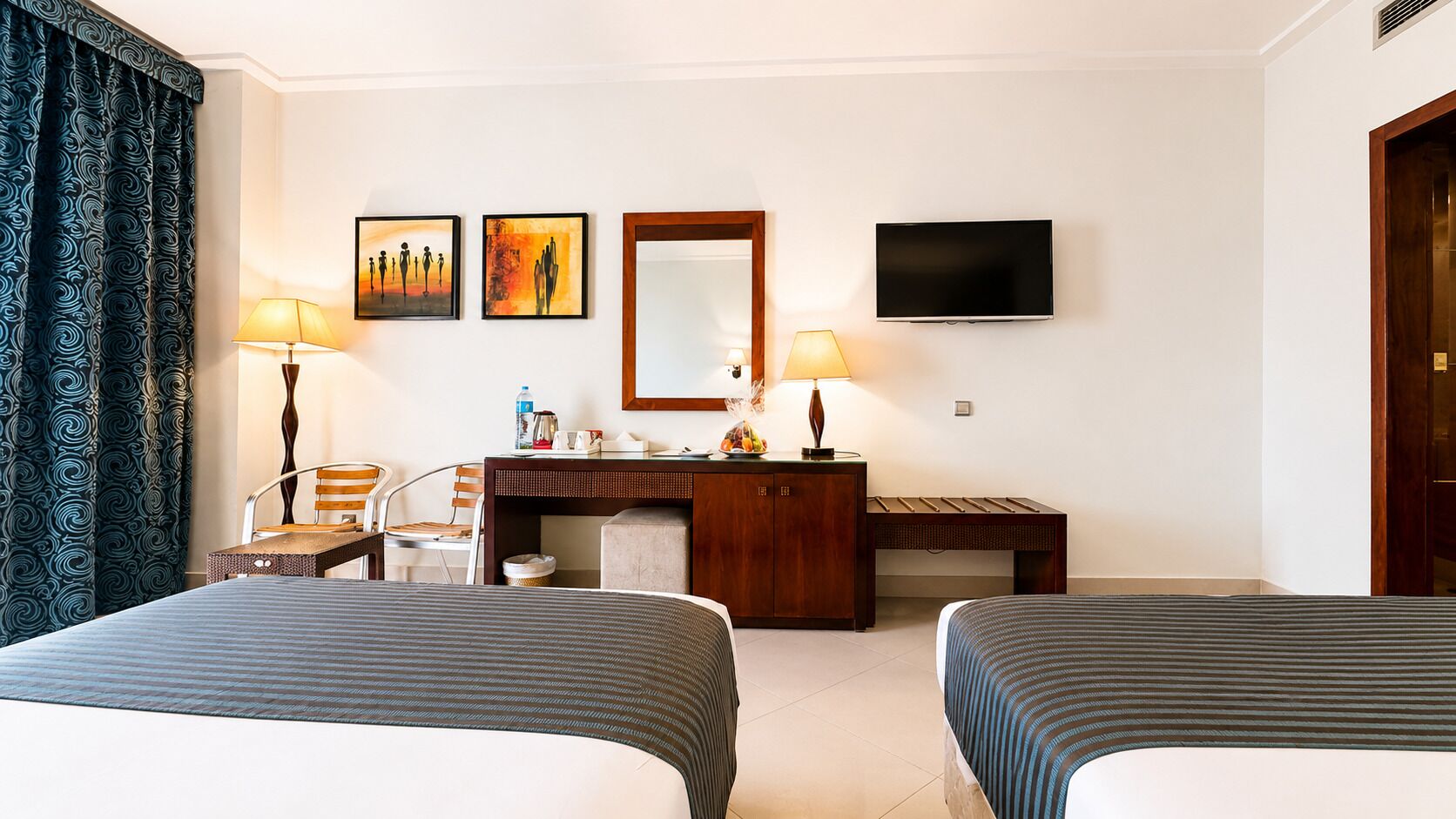 Une chambre d’hôtel avec deux lits, un bureau, une chaise, une télévision et des œuvres d’art accrochées au mur.