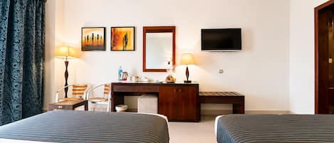 Une chambre d’hôtel avec deux lits, un bureau, une chaise, une télévision et des œuvres d’art accrochées au mur.