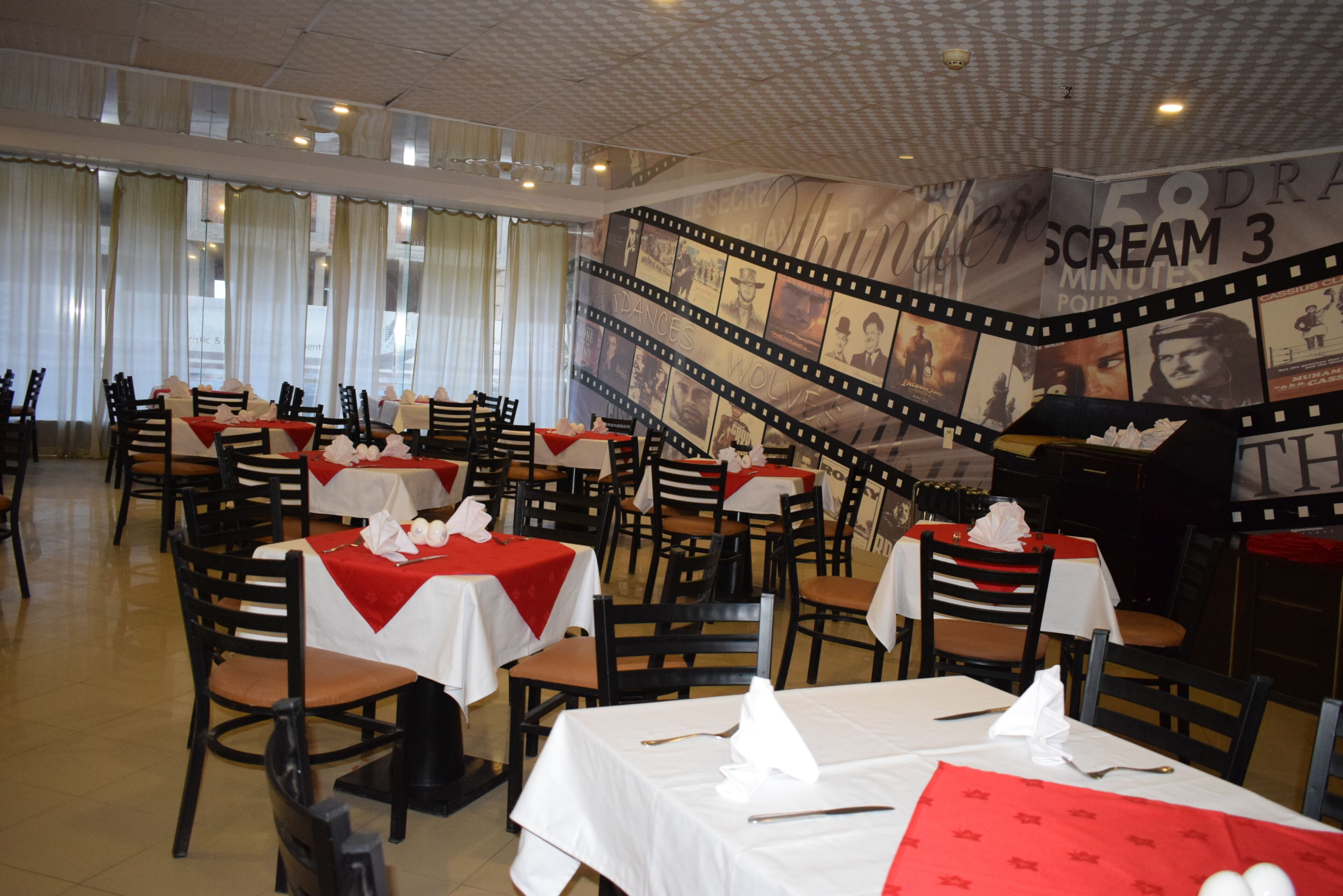 A restaurant with tables set for dining, a film strip mural on the wall, and a view of the street outside.