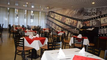 Un ristorante con tavoli apparecchiati, un murale a tema film e vista sulla strada.
