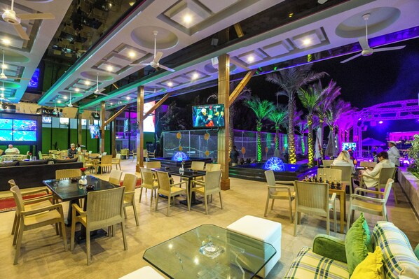 A spacious indoor area with multiple seating arrangements, including tables and chairs, and a bar area with a television screen.