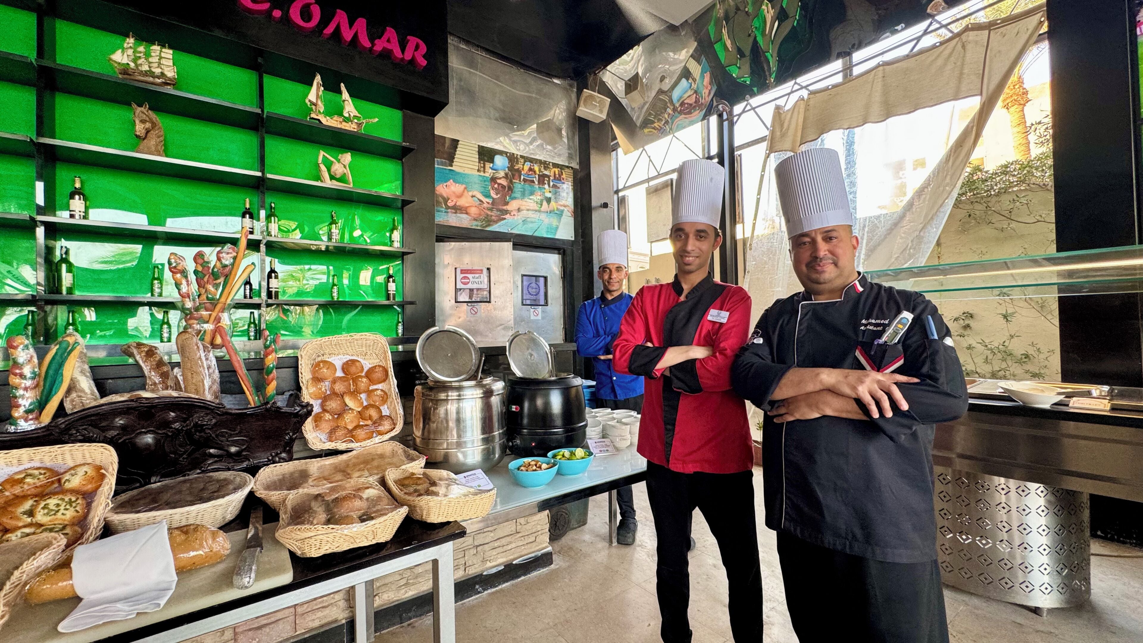 Een bakkerij met schappen vol brood en gebak, een toonbank met verse producten, en personeel in uniform.
