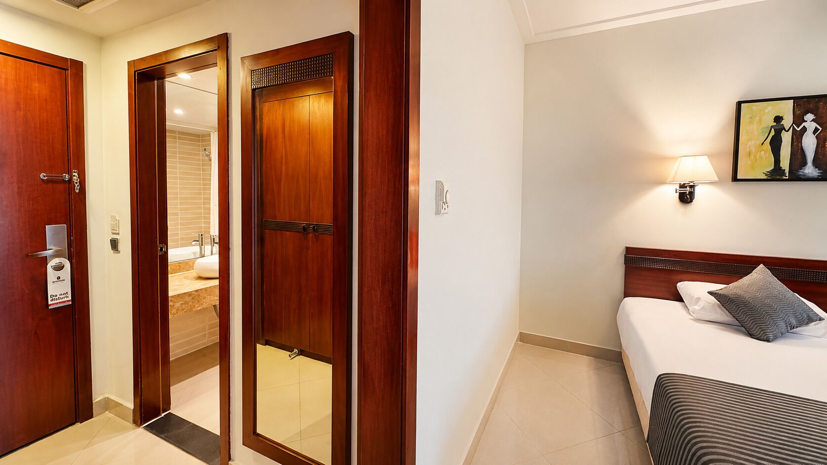 A hotel room with a bed, a nightstand, a wall-mounted lamp, and a painting.