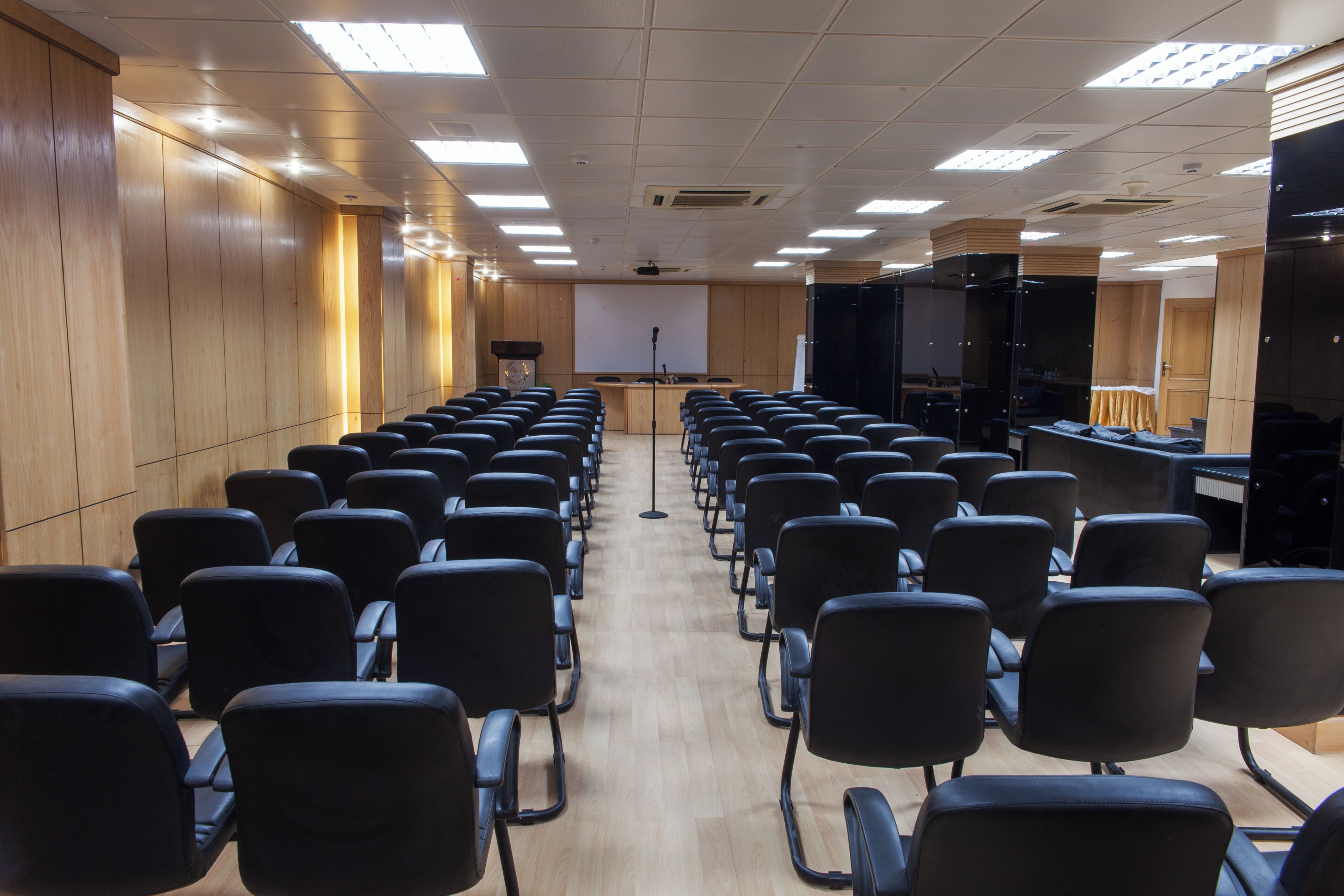 Une salle de conférence avec des rangées de chaises, un pupitre, un écran de projection et un écran noir sur le côté droit.