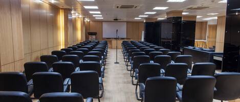 A conference room with rows of chairs, a podium, a projector screen, and a black screen on the right.