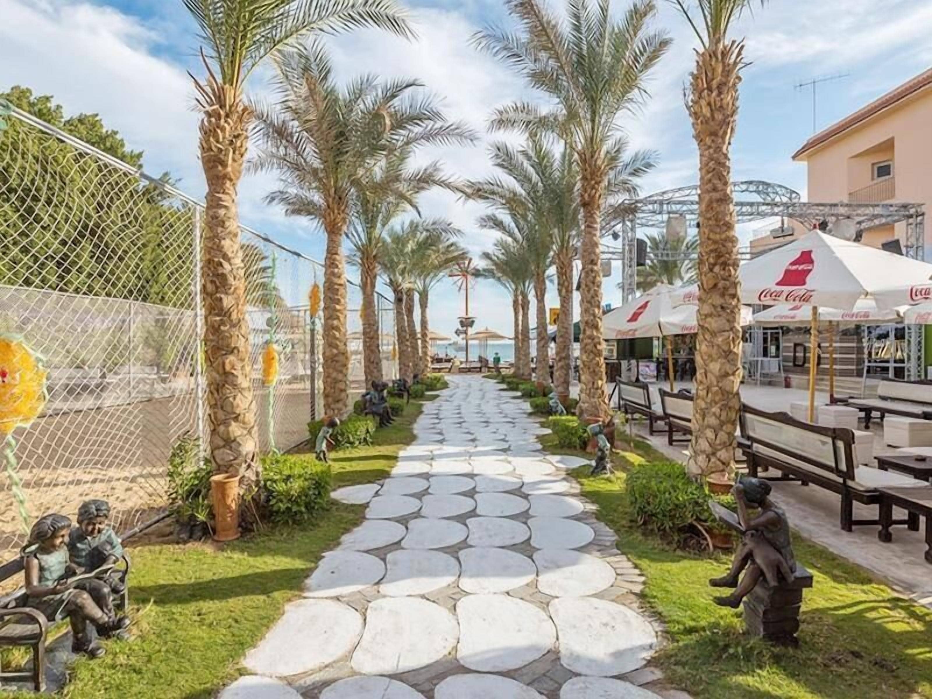 Un sentier bordé de palmiers, agrémenté de bancs et de coins salons extérieurs avec des parasols.