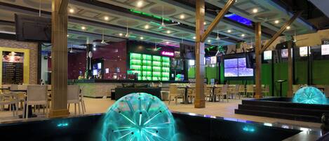 A modern indoor space with a bar area, seating, and a unique illuminated water feature.
