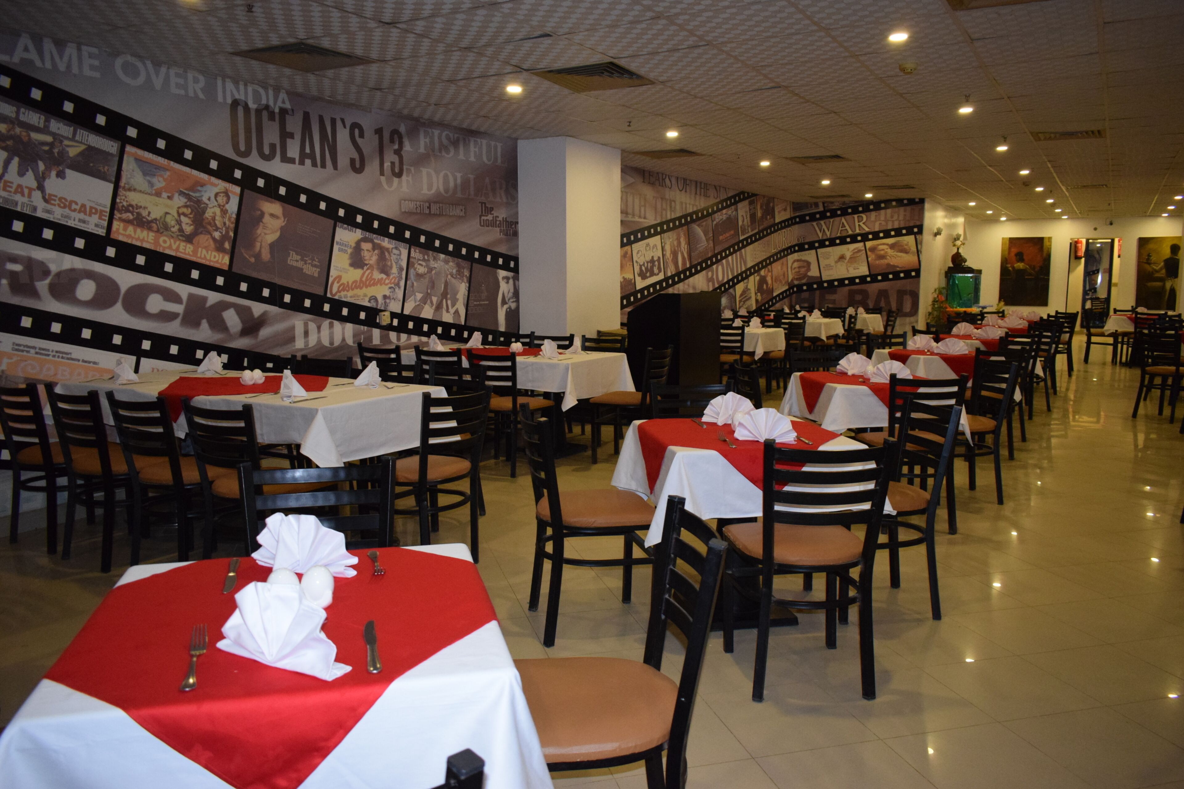 A restaurant with multiple tables and chairs, a film strip wall decoration, and a tiled floor.