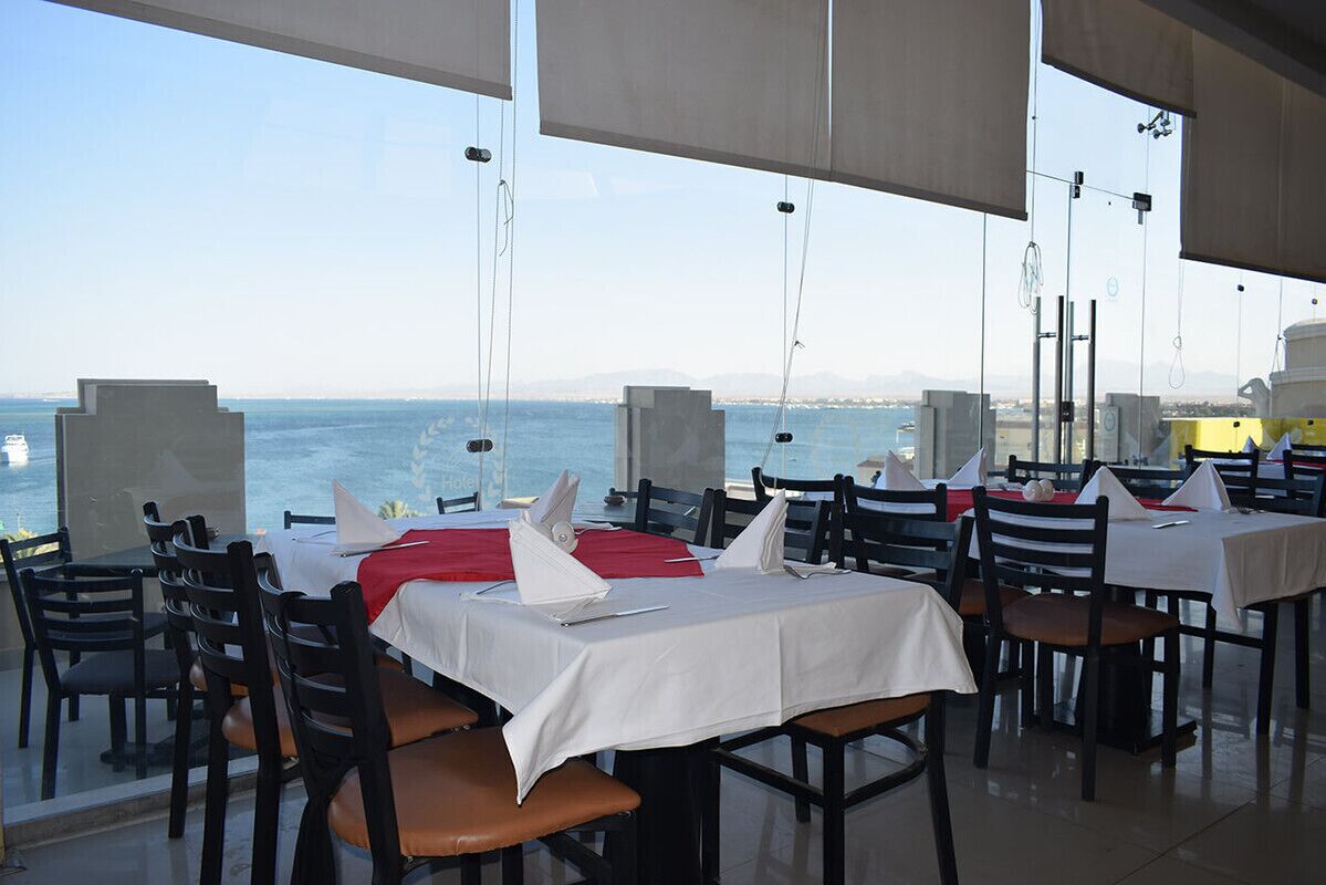 A restaurant with tables set for dining, a view of the sea, and a clear sky.