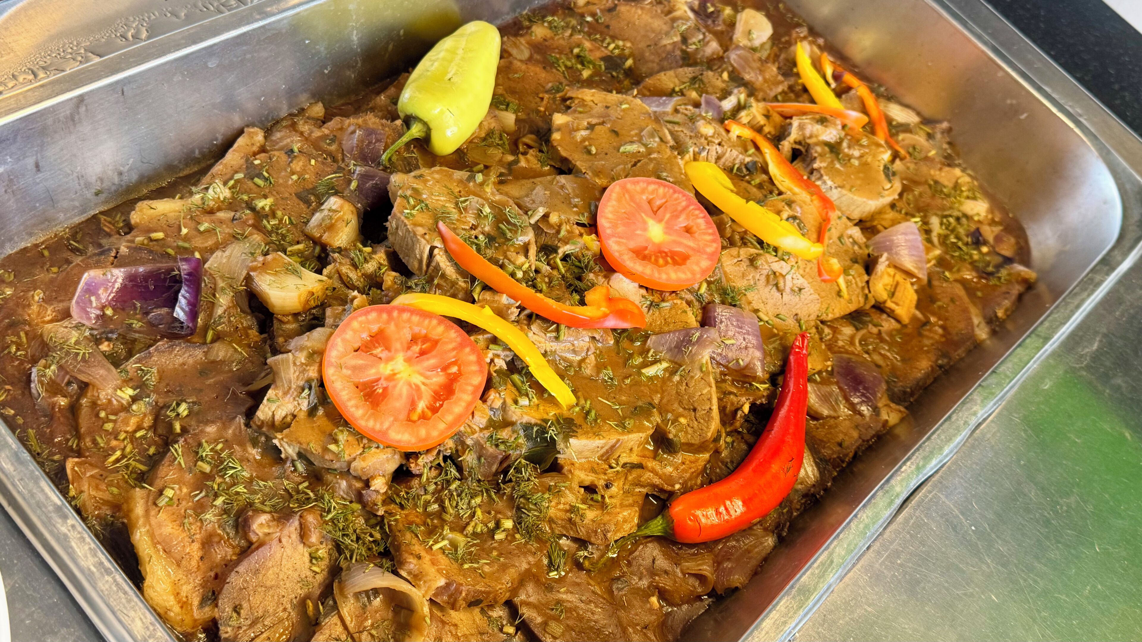 Un plat composé de viande, de légumes et d’herbes aromatiques, servi dans un récipient en métal.