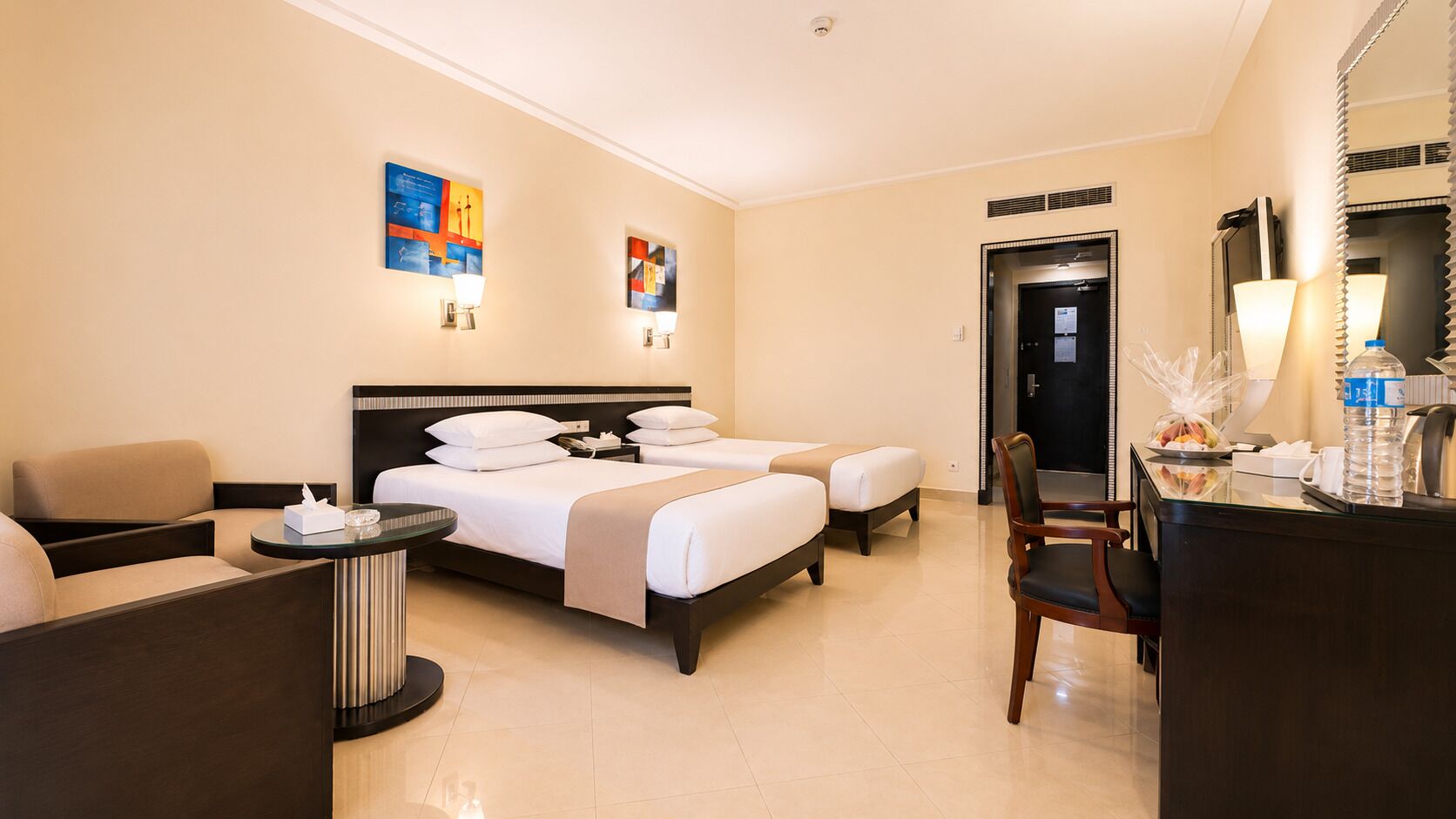 Een hotelkamer met een bed, twee nachtkastjes, een bureau, een stoel en een receptiehoek.