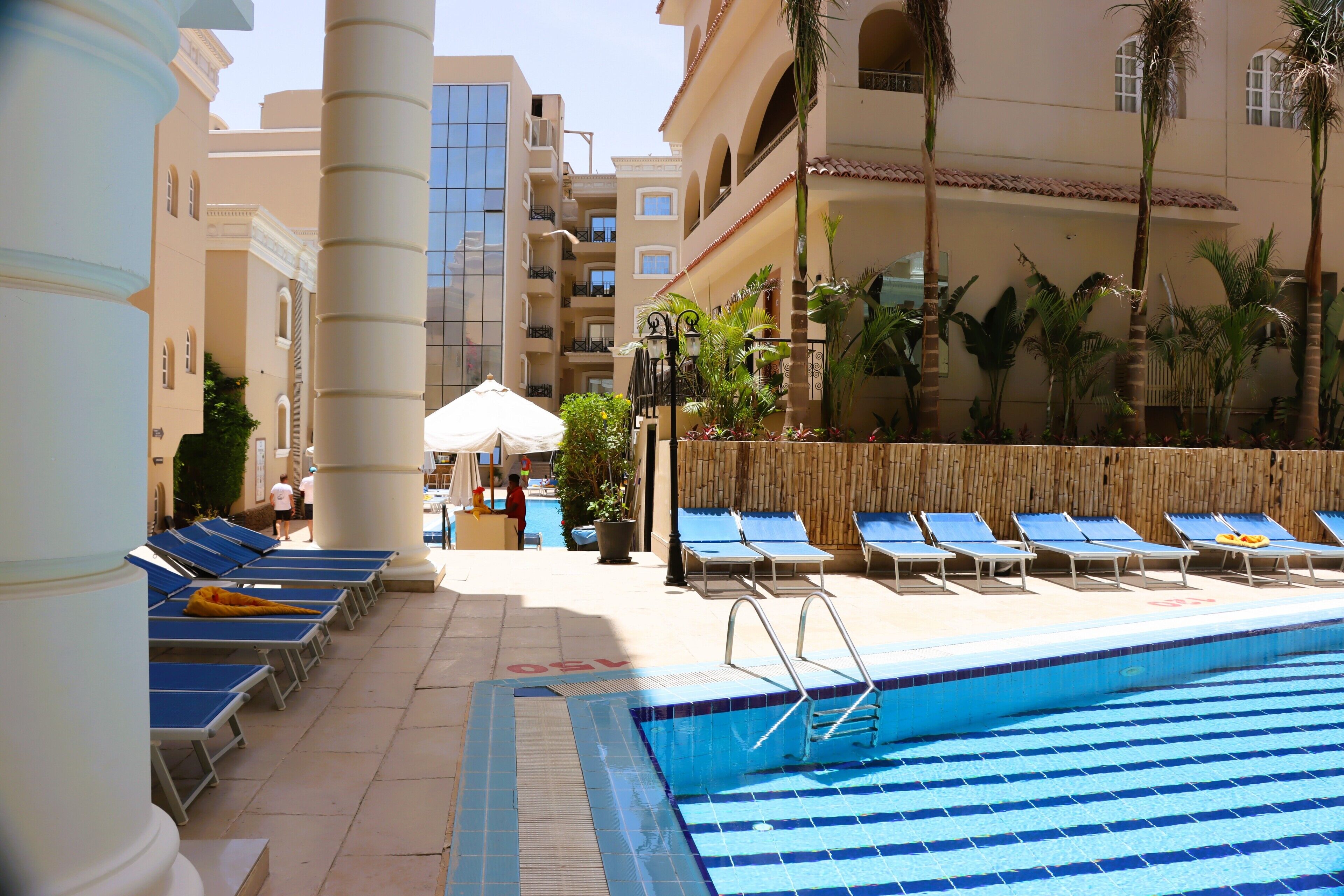 Un espace piscine comprenant des chaises longues, une piscine et un bâtiment doté de balcons.