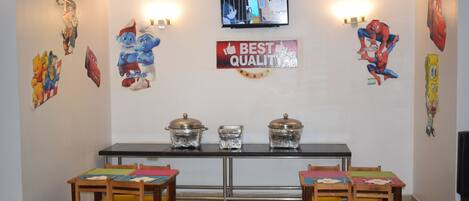 A dining area with a table, chairs, and wall decorations including cartoon characters and a 'Best Quality' sign.