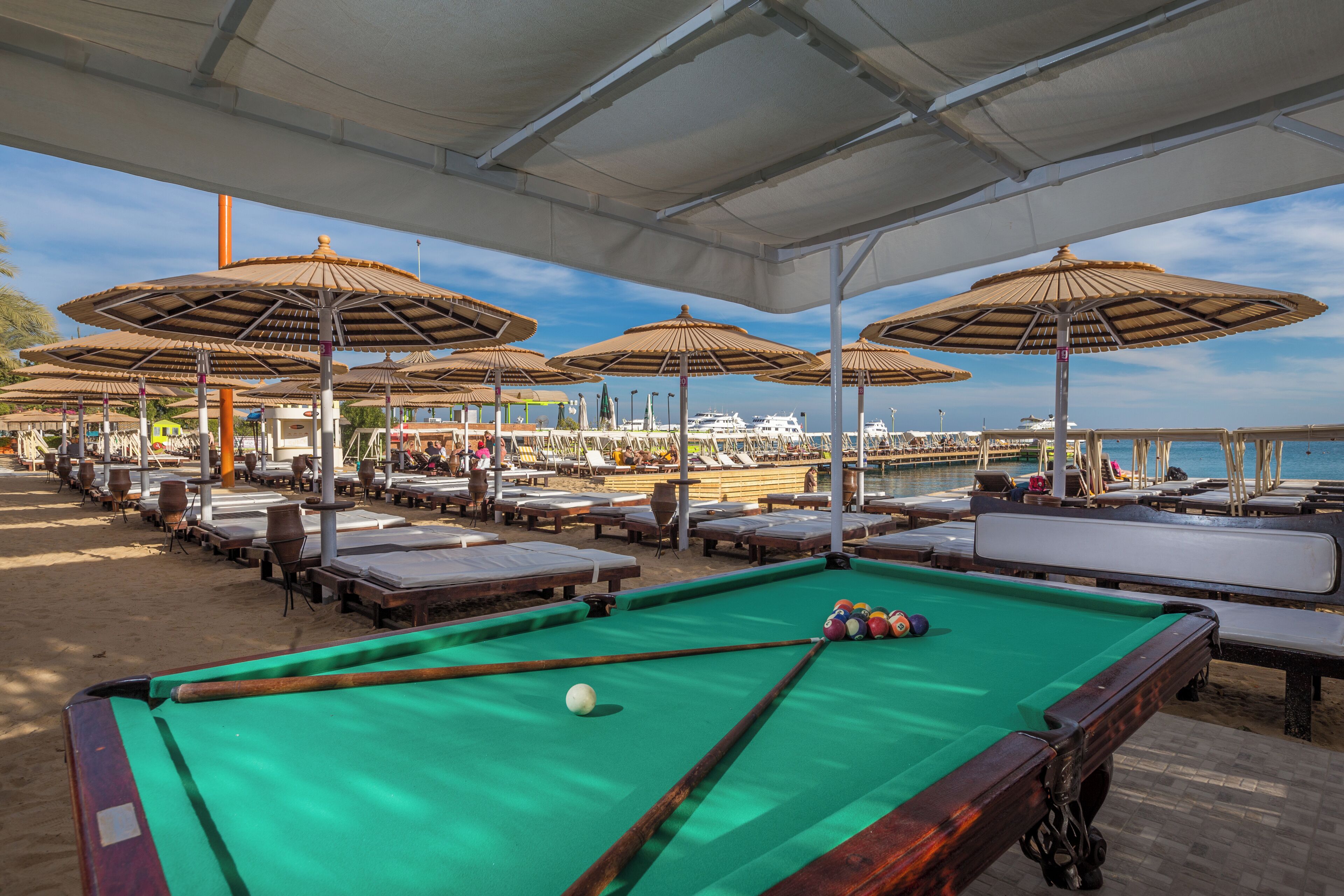 A pool table with a green felt surface, surrounded by lounge chairs and umbrellas.