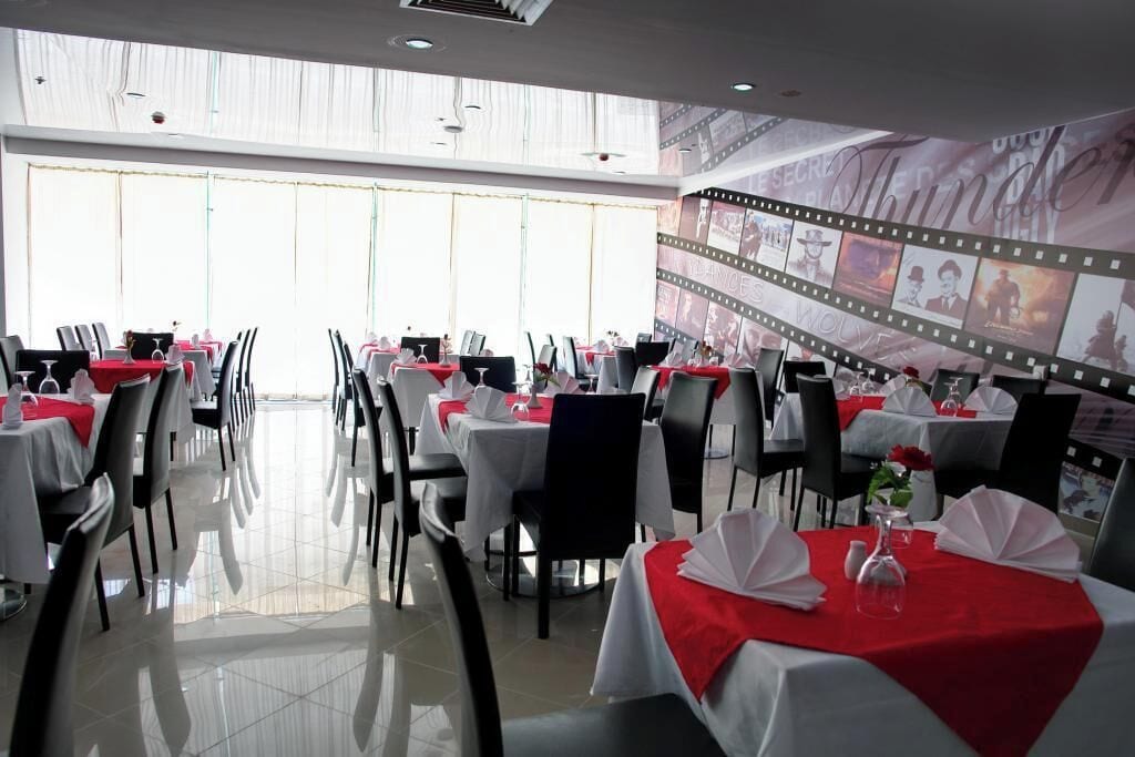 A restaurant with tables set for dining, a large window, and a film strip wall decoration.