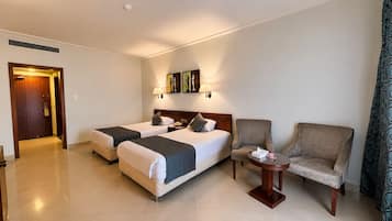 A hotel room with two beds, a chair, a small table, and artwork on the wall.