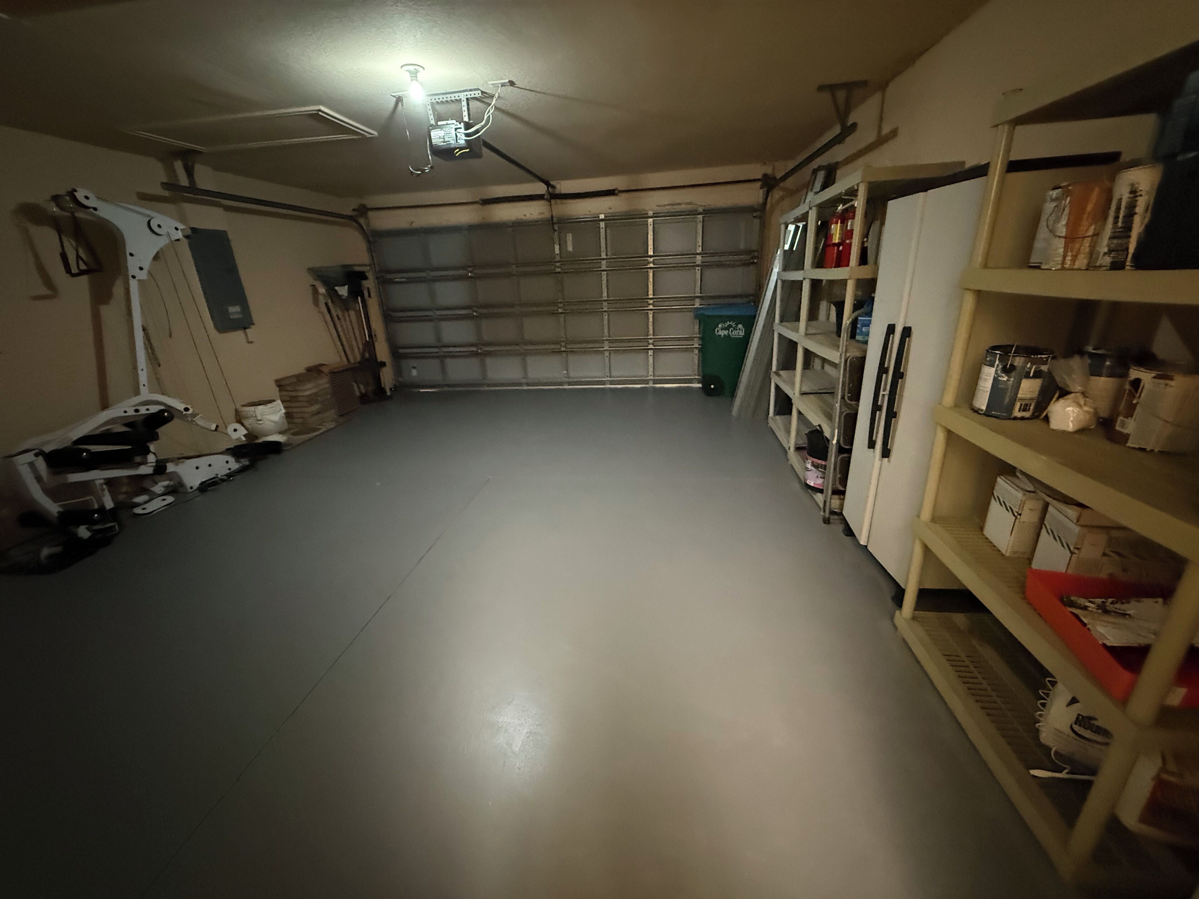 Eine Garage mit Betonboden, Deckenventilator und Regalen rechts, die verschiedene Gegenstände beherbergen.