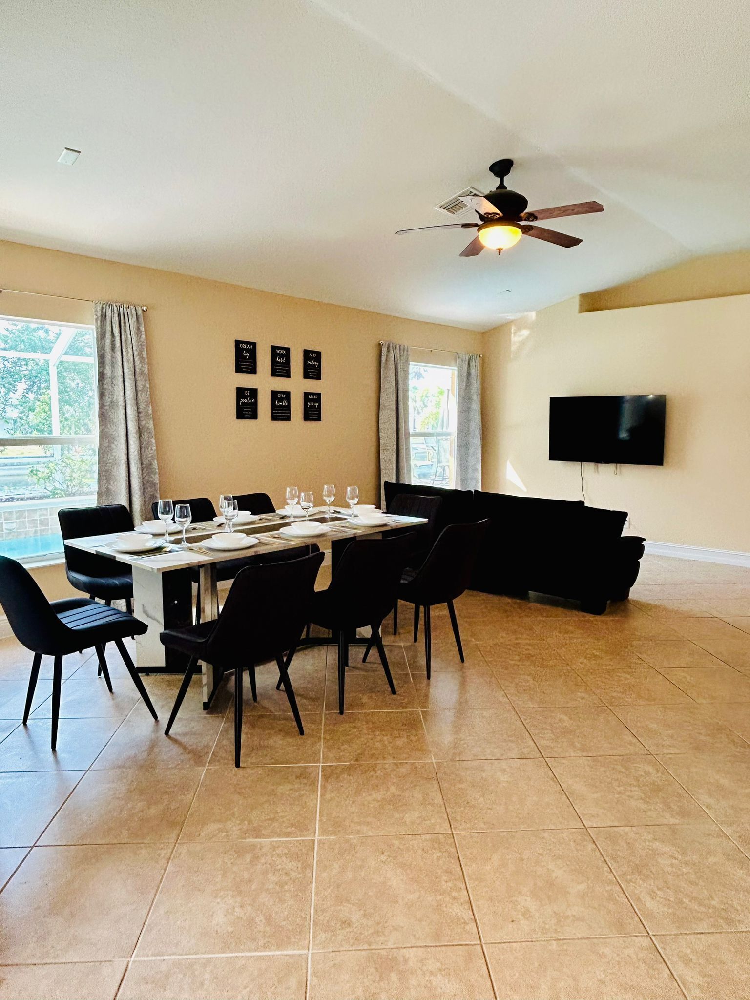 Un coin repas avec une table dressée pour quatre personnes, des chaises noires, un ventilateur de plafond et un téléviseur fixé au mur.