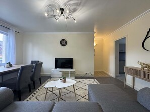 Una sala de estar moderna con un televisor de pantalla plana, sofás grises, una mesa de comedor con sillas, una araña y una pequeña decoración de elefante.