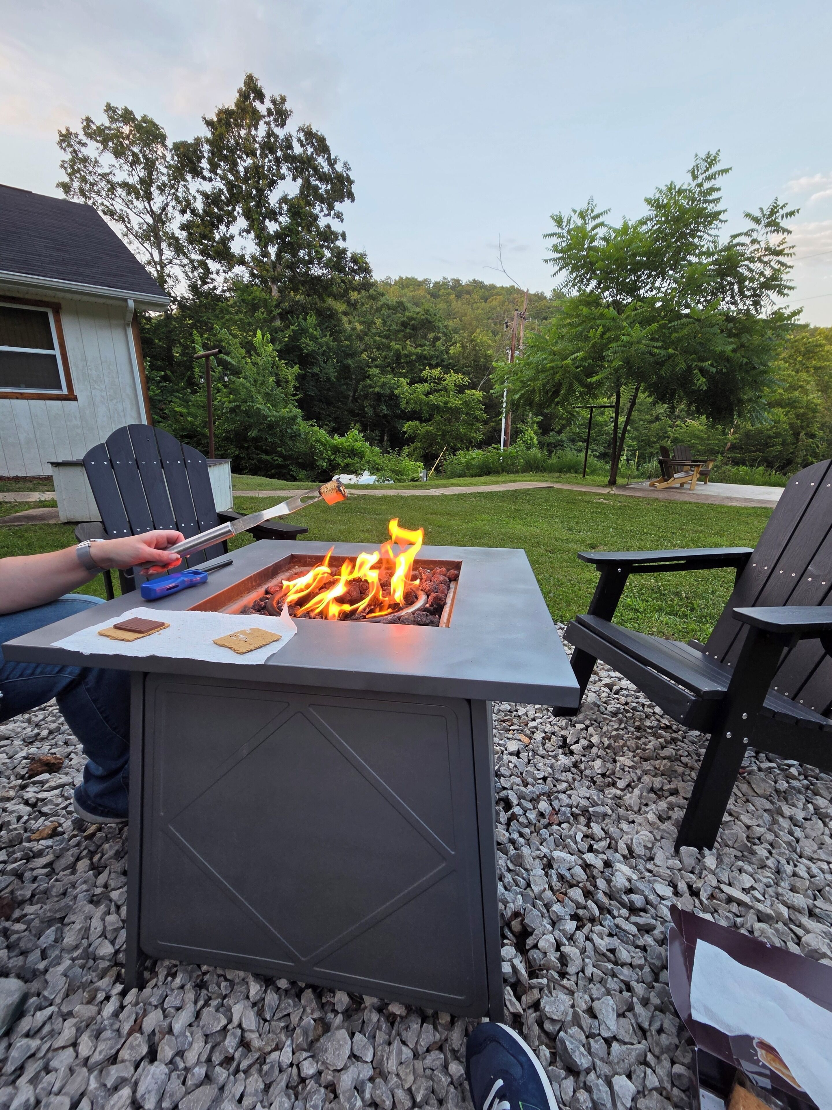 A fire pit with a metal table in front, surrounded by outdoor seating and a grassy area.