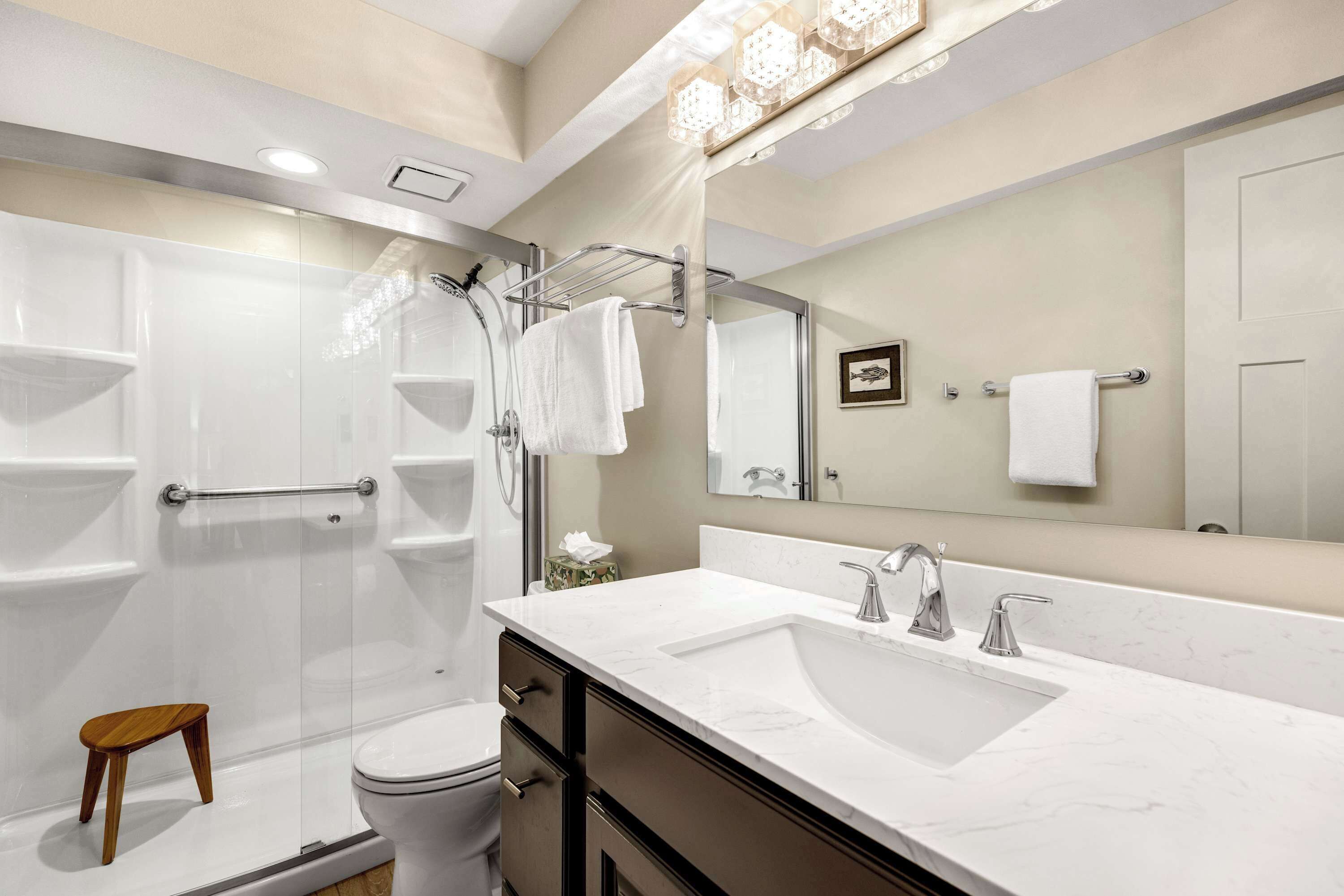 A modern bathroom with a glass-enclosed shower, a white sink, and a large mirror.