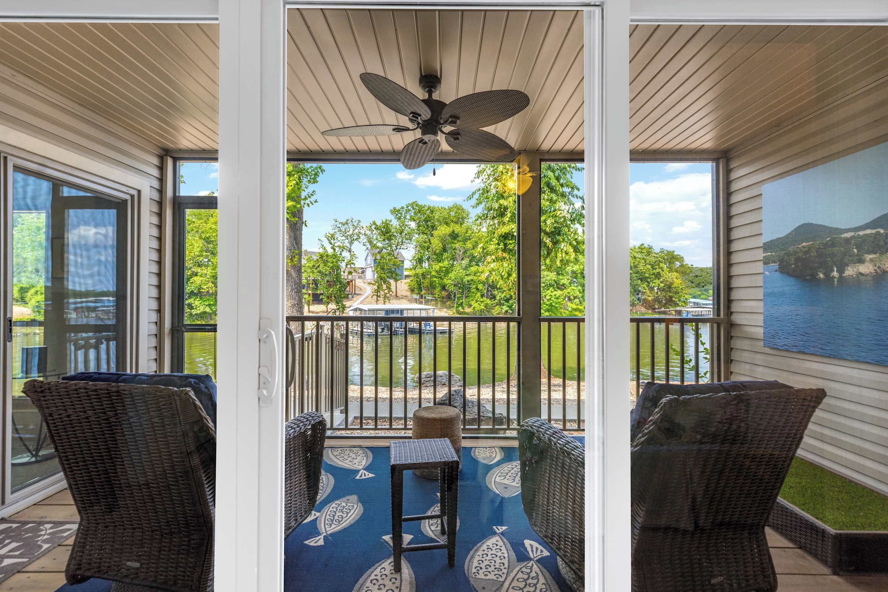 A covered patio with wicker furniture, a ceiling fan, and a view of a lake and greenery.