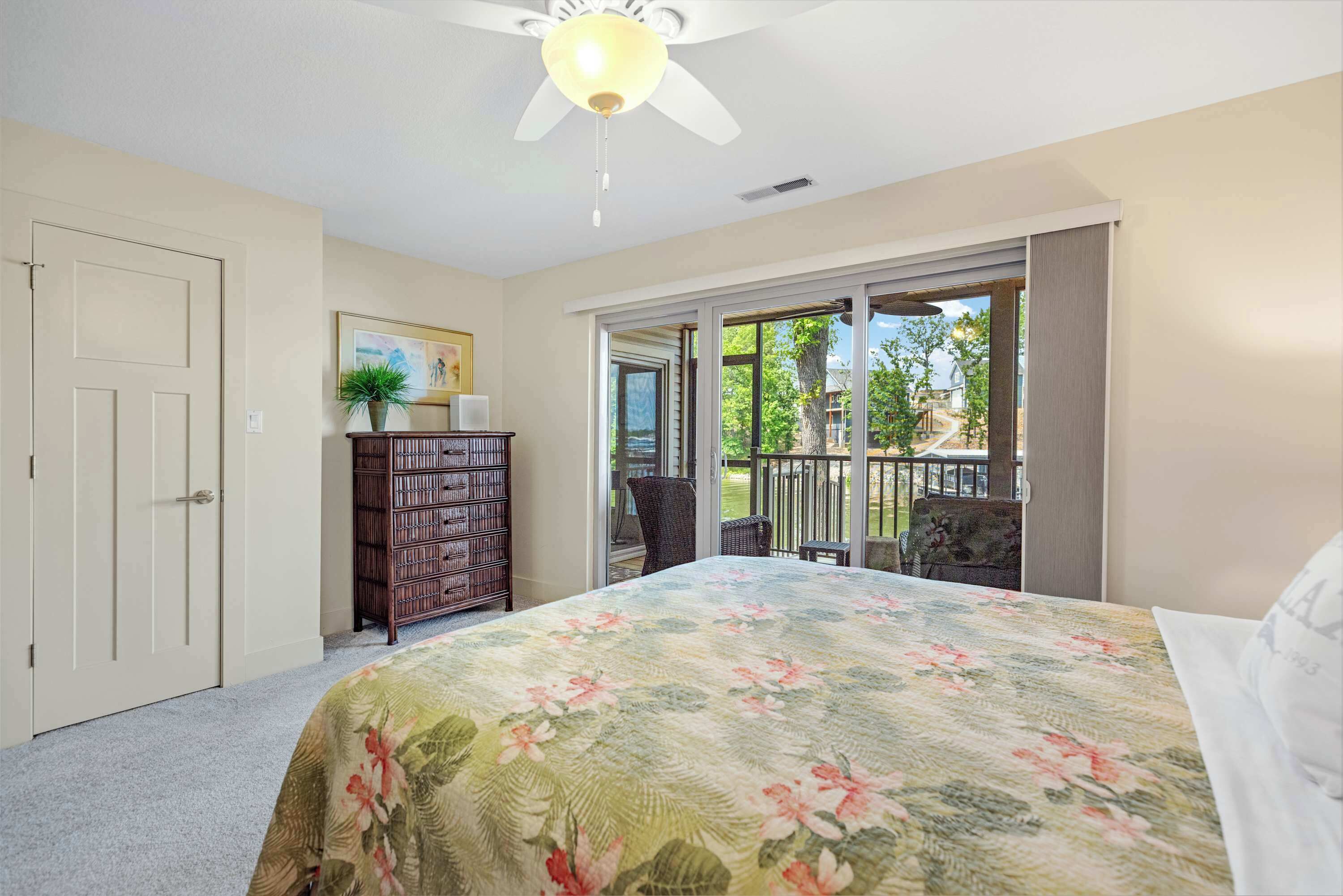 A bedroom with a bed, a dresser, a chair, and a balcony with a view of the outdoors.