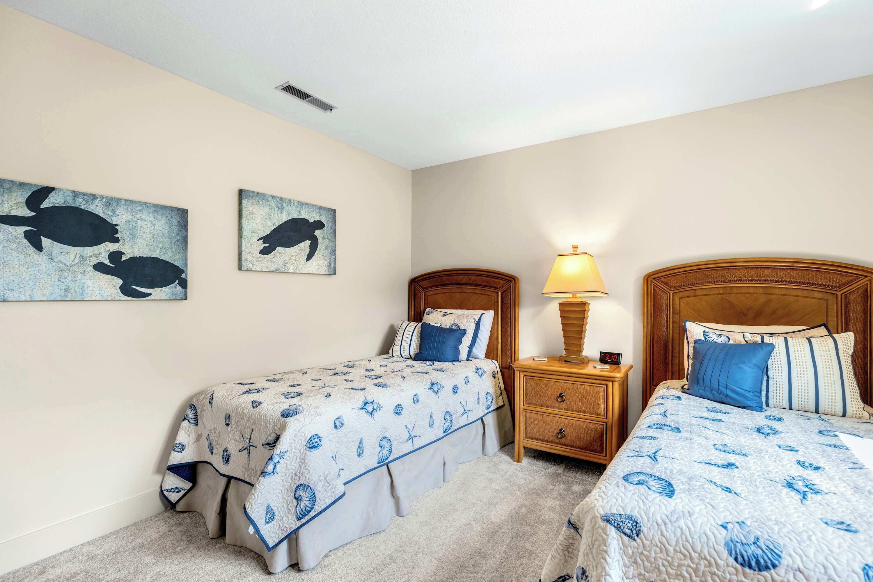 A bedroom with two beds, a nightstand with a lamp, and two wall-mounted artwork depicting sea turtles.