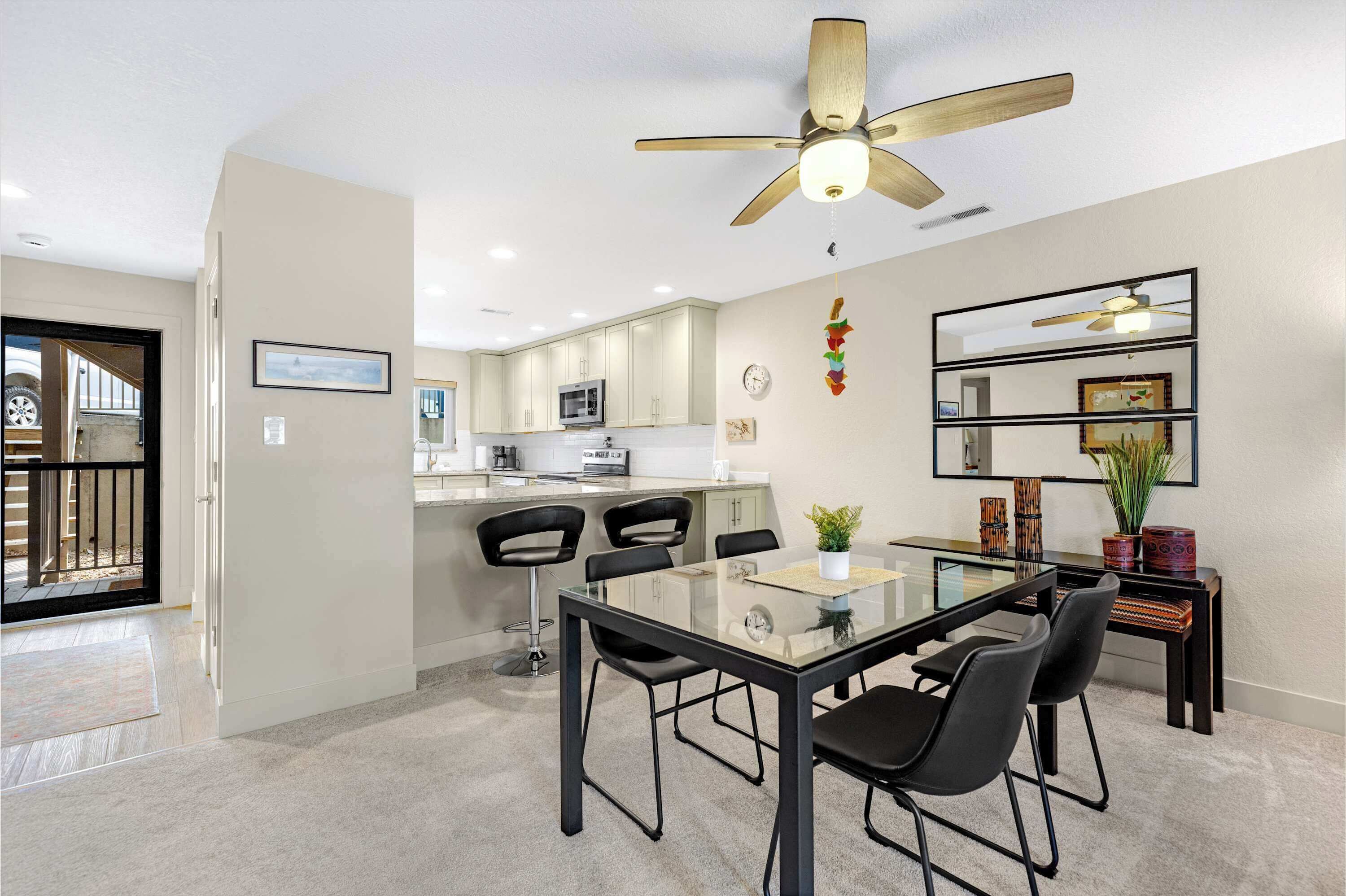 Una cucina moderna con mobili bianchi, un'area pranzo con tavolo in vetro e sedie nere, e una ventola a soffitto.