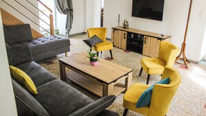 Een woonkamer met een bank, fauteuils, een salontafel en een televisie.