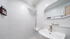 A modern bathroom with white speckled tiles, a shower, a sink, and a mirror.