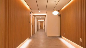 A modern hotel corridor with wooden paneling on the walls, a light fixture, and a sign indicating the direction to the lobby.